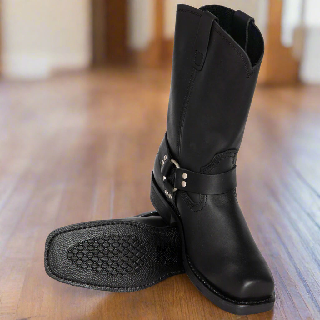 Black leather boot with a strap on a wooden floor